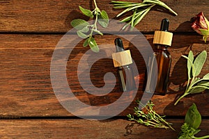Bottles of essential oil and fresh herbs on wooden table, flat lay. Space for text