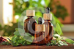 Bottles of essential oil and fresh herbs on wooden table in room