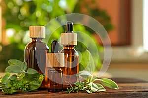 Bottles of essential oil and fresh herbs on wooden table in room. Space for text