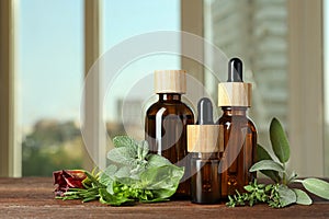 Bottles of essential oil and fresh herbs on wooden table in room. Space for text