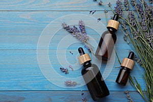 Bottles of essential oil and lavender flowers on light blue wooden table, flat lay. Space for text