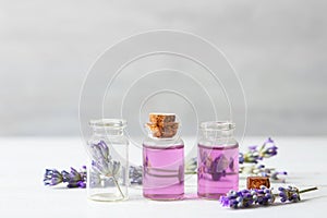 Bottles with essential oil and lavender flowers on white table