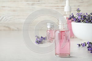 Bottles of essential oil and lavender flowers on white wooden table