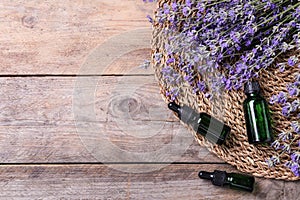 Bottles of essential oil and lavender flowers on wooden background. Space for text