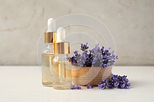 Bottles of essential oil and lavender flowers on wooden table