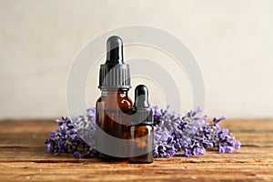 Bottles of essential oil and lavender flowers on wooden table