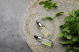 Bottles of essential oil and mint on grey table, top view. Space for text