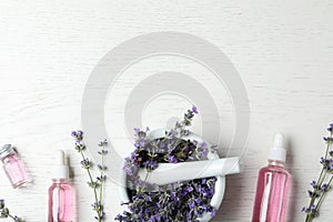 Bottles of essential oil, mortar and  with lavender flowers on white wooden background, flat lay. Space for text