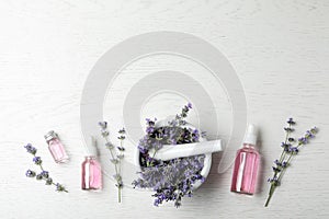Bottles of essential oil,  and pestle with lavender flowers on white wooden background, flat lay. Space for text