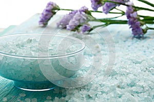 Bottles essential oil and sea salt on a blue wooden table, with flowers