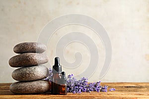 Bottles of essential oil, spa stones and lavender flowers on wooden table. Space for text