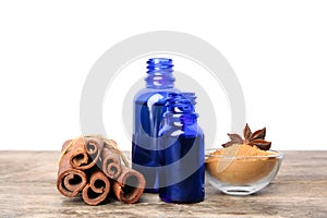 Bottles of essential oils, cinnamon sticks and powder on wooden table against whit