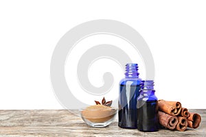 Bottles of essential oils, cinnamon sticks and powder on wooden table against white background