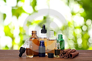 Bottles of essential oils and cinnamon sticks on table against blurred background