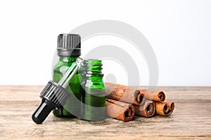 Bottles of essential oils and cinnamon sticks on wooden table against white