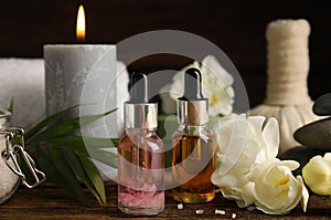 Bottles with essential oils and flowers on wooden table. Spa products