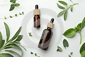 Bottles of essential oils and fresh herbs on white marble table, flat lay