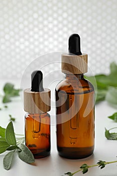 Bottles of essential oils and fresh herbs on white table