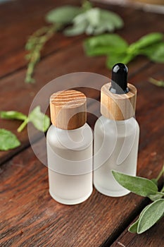 Bottles of essential oils and fresh herbs on wooden table