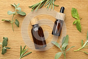 Bottles of essential oils and fresh herbs on wooden table, flat lay