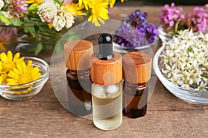 Bottles of essential oils and many beautiful flowers on wooden table