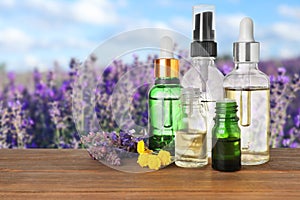 Bottles of essential oils and wildflowers on table against blurred background. Space for text