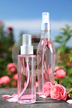 Bottles of facial toner with essential oil and fresh roses on table against blurred