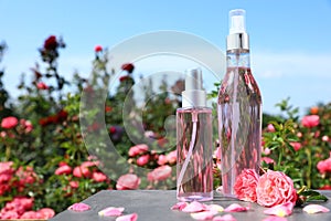 Bottles of facial toner with essential oil and fresh roses on table against blurred background.