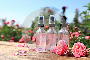 Bottles of facial toner with essential oil and fresh roses on wooden table