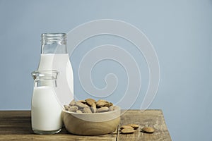 Bottles of fresh milk with almonds on wooden table on light blue background
