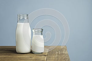 Bottles of fresh milk on wooden table on light blue background