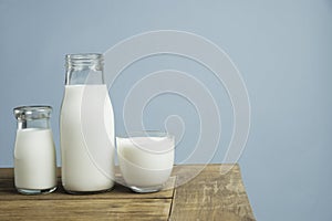 Bottles of fresh milk on wooden table on light blue background