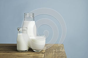 Bottles of fresh milk on wooden table on light blue background