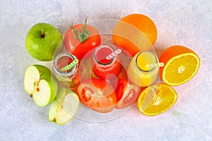 Bottles with fresh orange, apple, tomato juice and colored tubules on a gray concrete table. Top view.