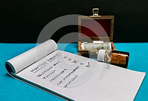 Bottles of glass homeopath medicine in wooden box and notepad on blue and dark background. Homeopathic medicine and Expenses