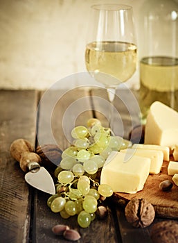 Bottles and glass of white wine, cheese, nuts and grapes