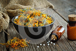 Bottles of homeopathic calendula granules, healthy marigold flowers in bowl and sack on wooden table. Homeopathy