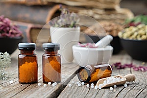 Bottles of homeopathic globules, books, mortars and bowls of healing herbs on background. Homeopathy photo