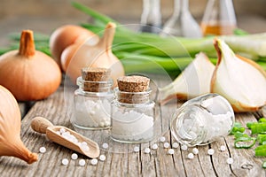 Bottles of homeopathic globules, onion bulbs and fresh green onions. Allium cepa homeopathic remedies