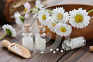 Bottles of homeopathy granules. Homeopathic remedy - Chamomilla. Daisies flowers in wooden bowl. Homeopathy medicine