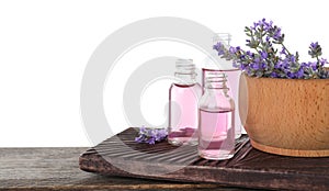Bottles of lavender essential oil and bowl with  flowers on wooden table against white background