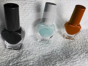 bottles with nail polish in black, light blue and orange, with white background towel photo