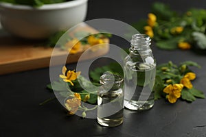 Bottles of natural celandine oil near flowers on black table