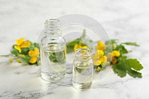 Bottles of natural celandine oil near flowers on white marble table