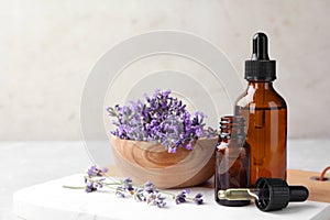 Bottles with natural essential oil and bowl of lavender flowers on table against light background