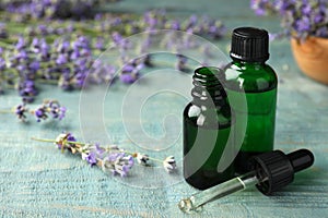Bottles with natural lavender essential oil on blue wooden background