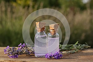 Bottles of natural lavender essential oil and flowers on wooden table outdoors