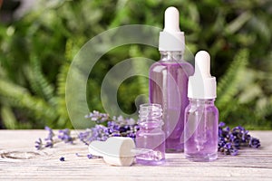 Bottles with natural lavender essential oil on white wooden table against blurred background.