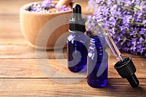 Bottles with natural lavender oil, dropper and flowers on wooden table, closeup view