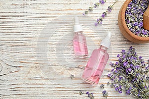 Bottles with natural lavender oil and flowers on white wooden table, flat lay